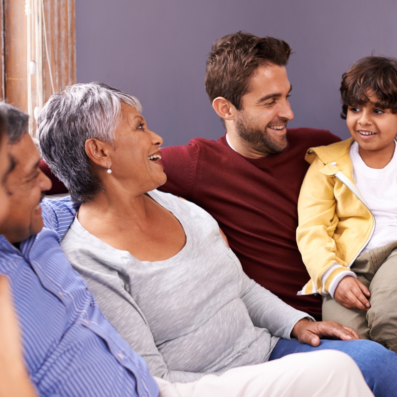 Grandparents, a father, and son are smiling while sitting together on a couch